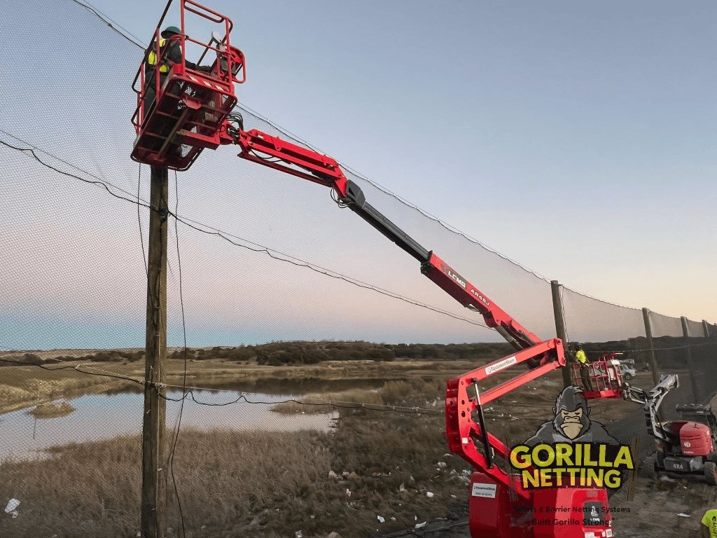 Crew installing tall litter-control netting on wooden poles at a landfill site using boom lifts