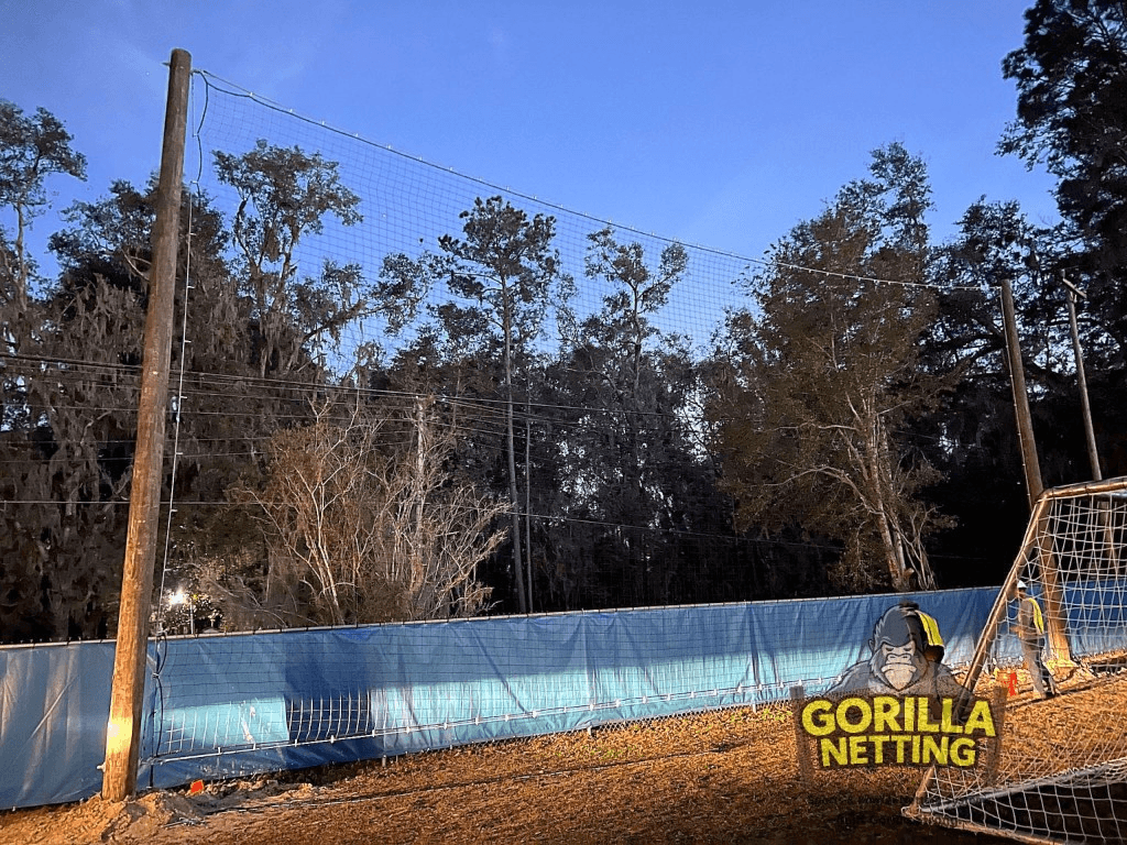 Soccer field perimeter netting at dusk with blue windscreen and tall support poles