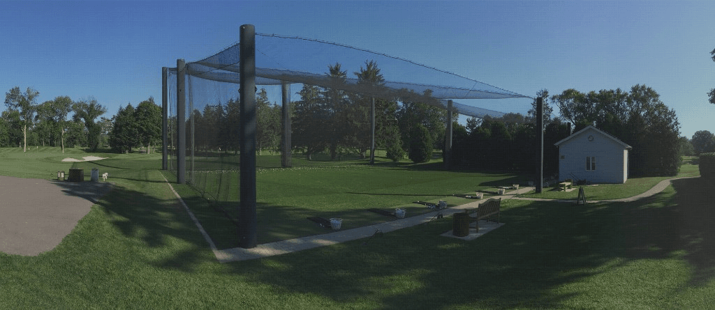 Panoramic view of a professional netted golf enclosure with overhead and side netting, hitting mats, and practice bays on a driving range