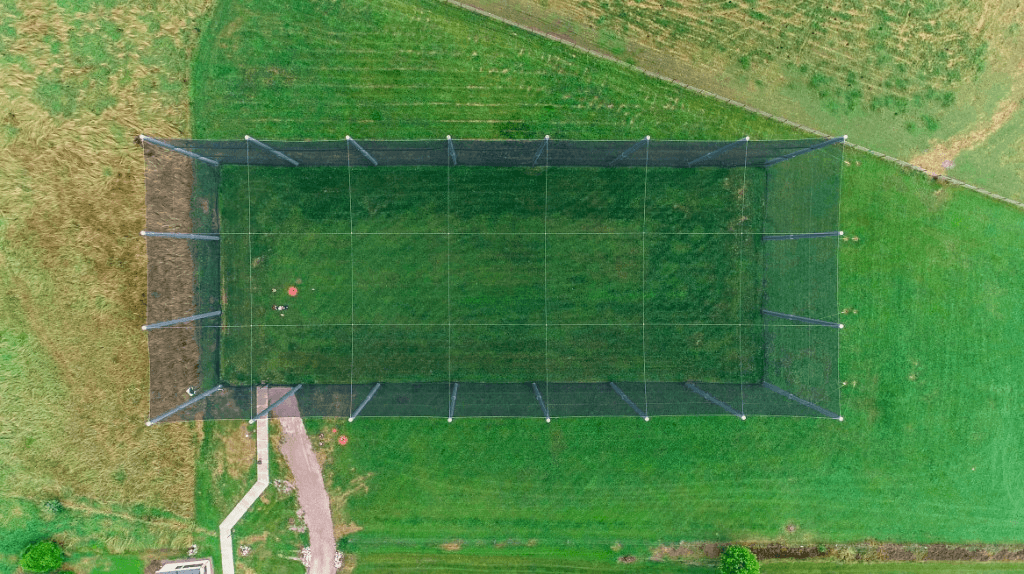 Overhead aerial view of a large rectangular netted drone enclosure on a grassy field